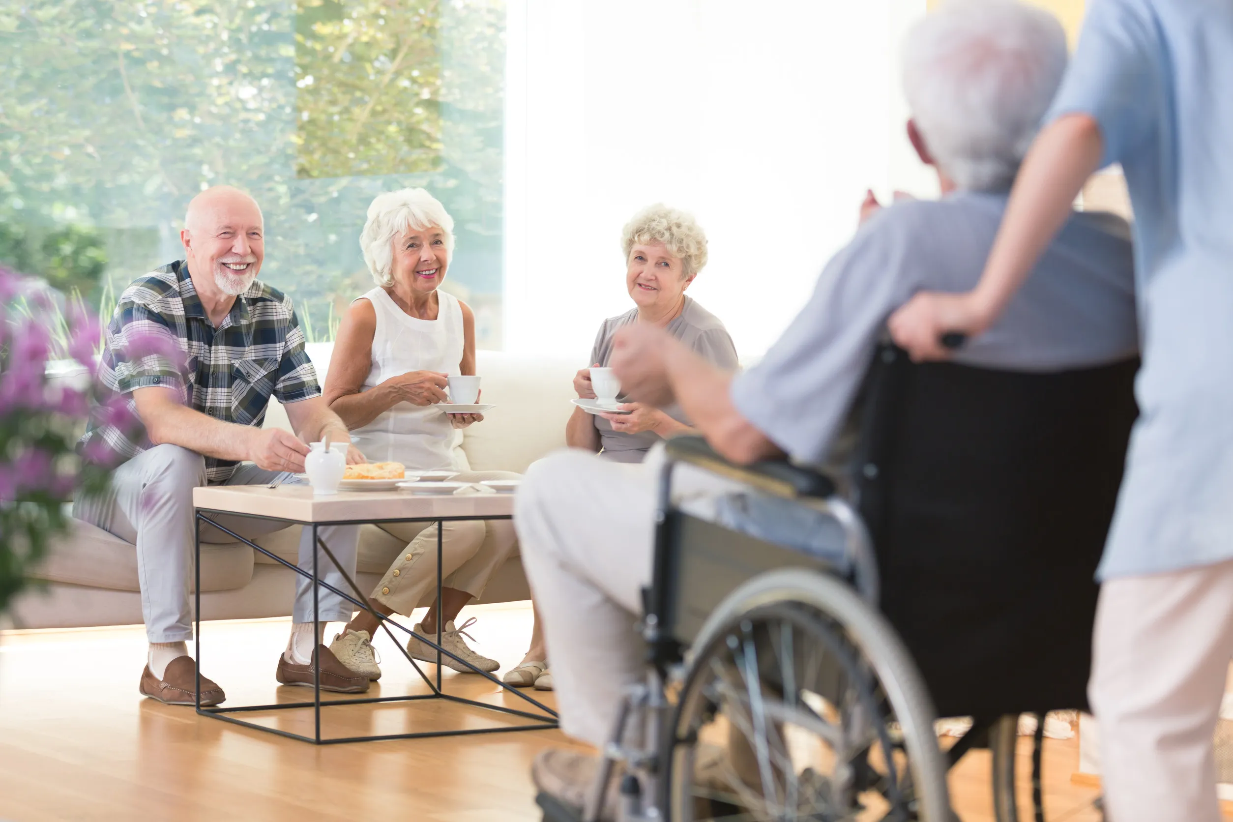 Happy seniors sitting on the couch and visiting their disabled friend at a nursing house